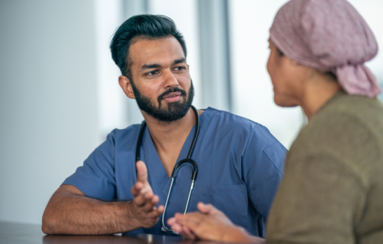 A male doctor wearing scrubs is talking to a woman wearing a head scarf. He appears to be explaining something to her.