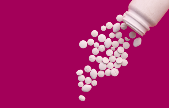 A plain white plastic pill bottle with about 40 different shaped and sized white pills spilling out of it.